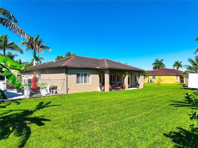 rear view of property featuring a lawn, a patio area, fence, and stucco siding