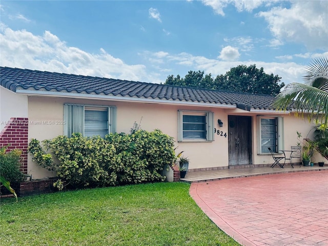 view of front of property featuring a tiled roof, a front lawn, and stucco siding