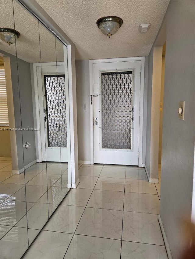 hall with a textured ceiling, tile patterned floors, and baseboards