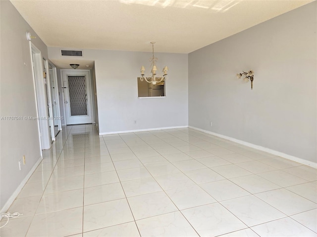 spare room with a chandelier, light tile patterned floors, visible vents, and baseboards