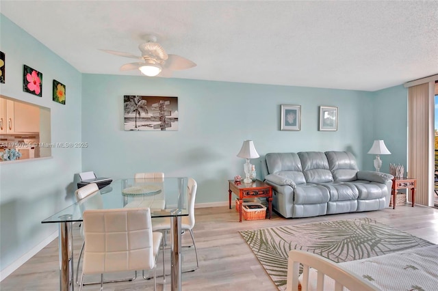 living room featuring a ceiling fan, light wood-type flooring, a textured ceiling, and baseboards