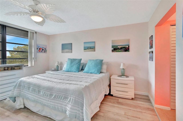 bedroom with light wood finished floors, ceiling fan, baseboards, and a textured ceiling