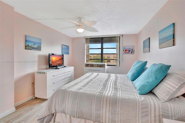 bedroom with a textured ceiling, baseboards, a ceiling fan, and light wood-style floors