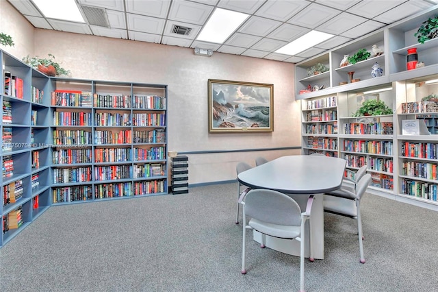 carpeted office space featuring wall of books, visible vents, and a drop ceiling