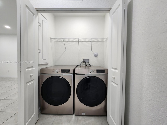 laundry room with light tile patterned floors, laundry area, washing machine and clothes dryer, and a textured wall