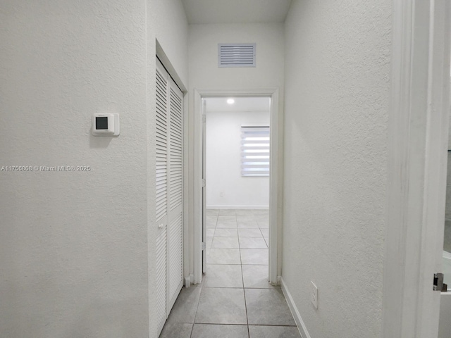 hallway with visible vents, a textured wall, baseboards, and light tile patterned floors