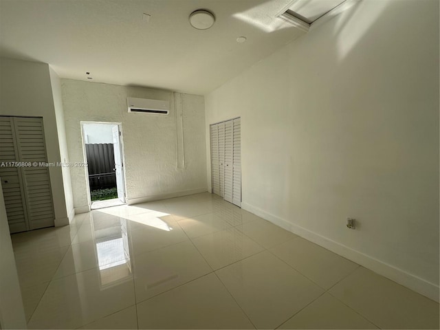 unfurnished bedroom with a wall unit AC, light tile patterned flooring, and baseboards