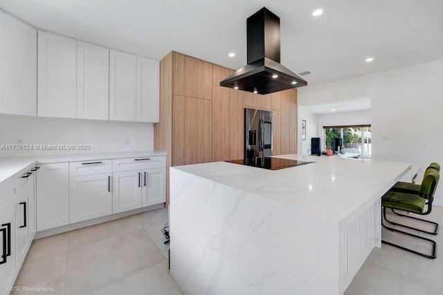 kitchen featuring light tile patterned floors, island range hood, light stone countertops, stainless steel fridge, and black electric cooktop