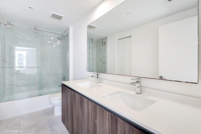 bathroom featuring toilet, combined bath / shower with glass door, a sink, and visible vents