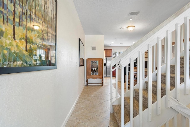 hallway with light tile patterned floors, a textured ceiling, stairs, and visible vents