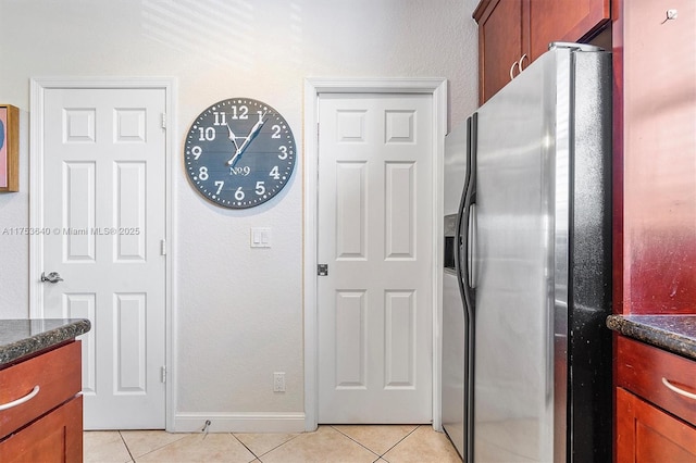 kitchen featuring light tile patterned floors, dark stone counters, stainless steel refrigerator with ice dispenser, and baseboards