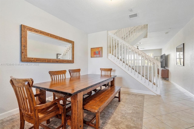 dining space with light tile patterned floors, a textured ceiling, visible vents, baseboards, and stairs