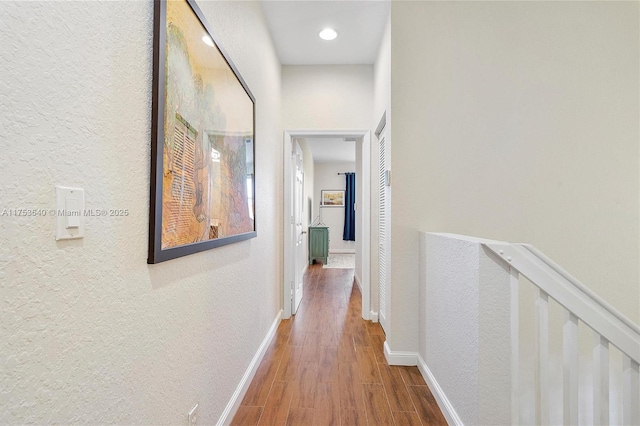 hall featuring baseboards, wood finished floors, and a textured wall