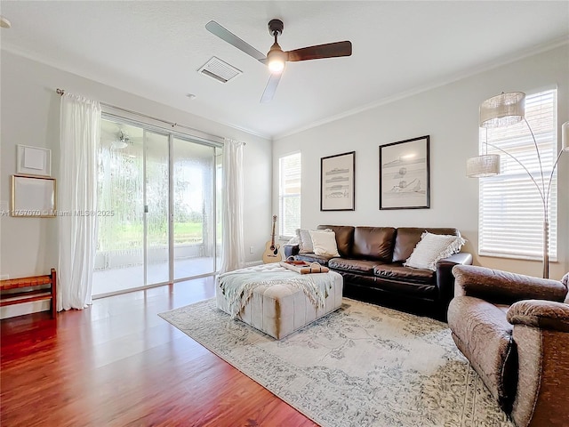 living room featuring a ceiling fan, visible vents, crown molding, and wood finished floors