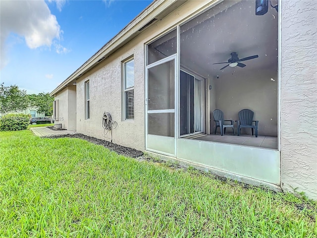 view of home's exterior with ceiling fan, a sunroom, a yard, and stucco siding