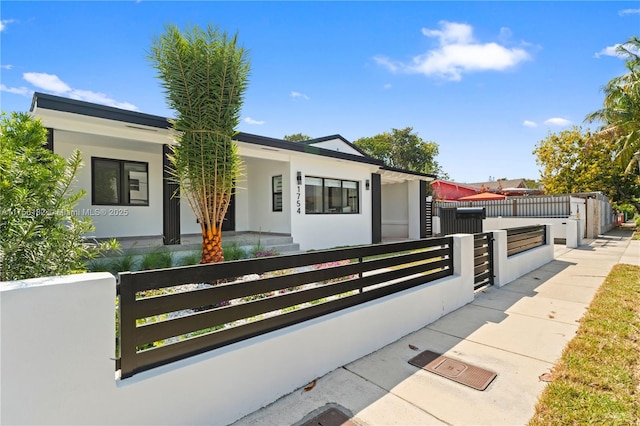 modern home with a porch, a fenced front yard, and stucco siding