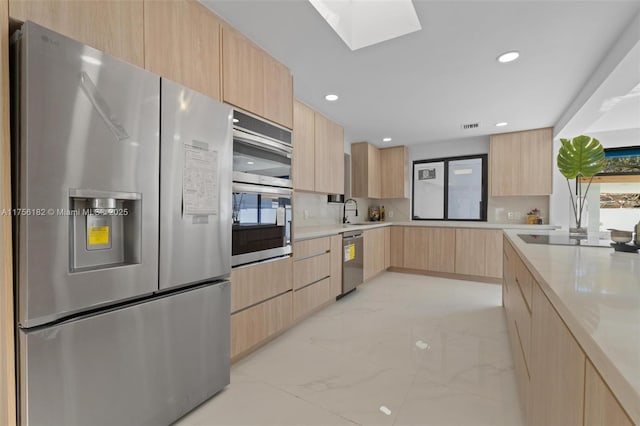 kitchen with stainless steel appliances, marble finish floor, modern cabinets, and light brown cabinetry