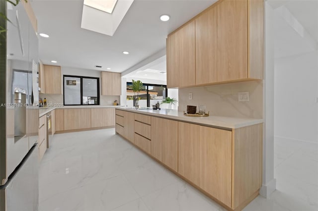 kitchen with light brown cabinets, light countertops, modern cabinets, a skylight, and marble finish floor