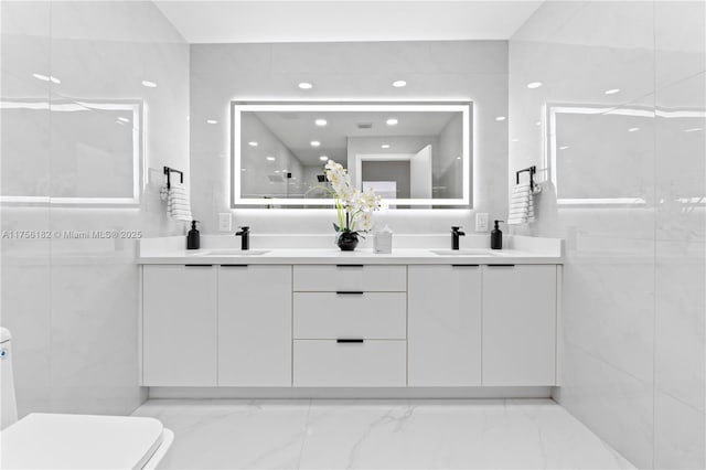 bathroom with double vanity, marble finish floor, a sink, and toilet