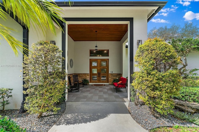 view of exterior entry featuring stucco siding, stone siding, and french doors