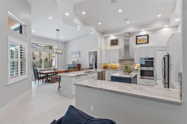 kitchen featuring a peninsula, appliances with stainless steel finishes, backsplash, wall chimney exhaust hood, and crown molding