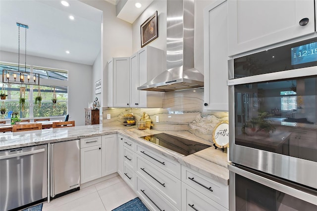 kitchen featuring stainless steel appliances, wall chimney range hood, light stone counters, and tasteful backsplash