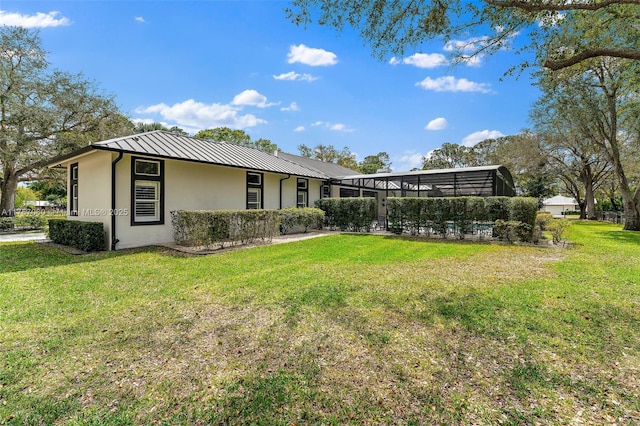 back of house featuring stucco siding, a lawn, a standing seam roof, glass enclosure, and metal roof