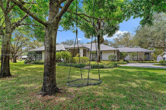 ranch-style home featuring a standing seam roof, metal roof, a front lawn, and stucco siding