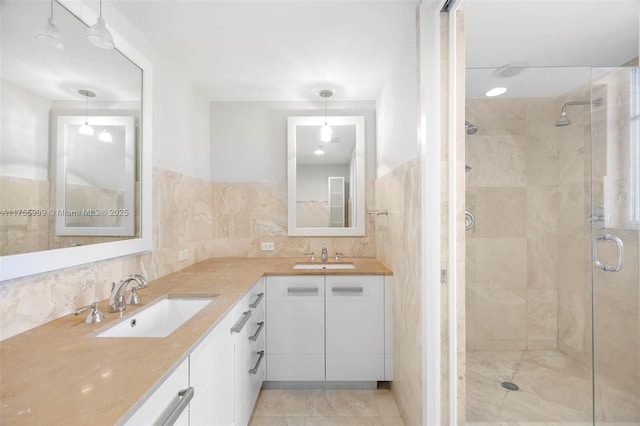 bathroom featuring double vanity, a shower stall, tile walls, and a sink