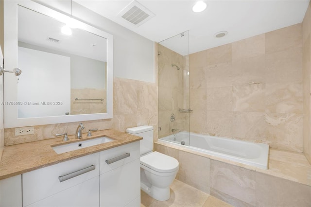 bathroom featuring tiled shower / bath, toilet, visible vents, and tile walls