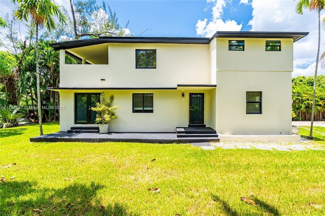 rear view of property with entry steps, a lawn, a balcony, and stucco siding