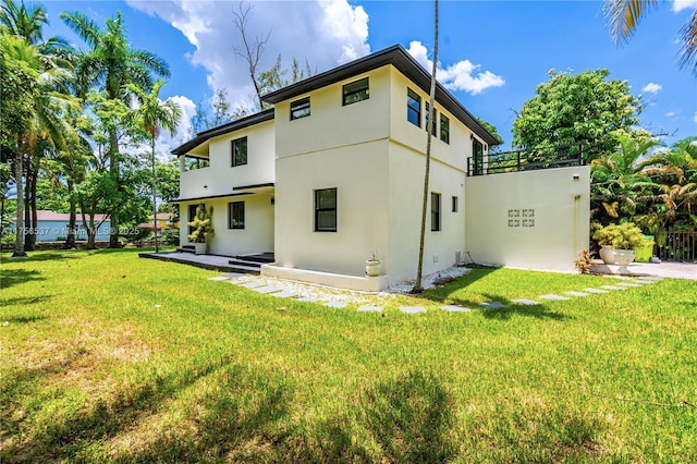 rear view of property featuring a lawn and stucco siding