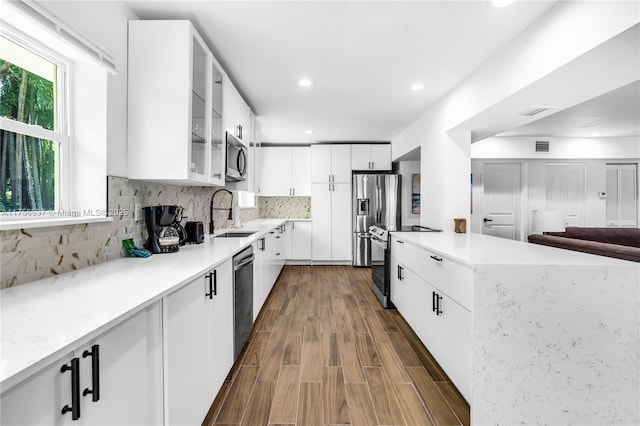 kitchen with stainless steel appliances, tasteful backsplash, dark wood-type flooring, white cabinetry, and a sink