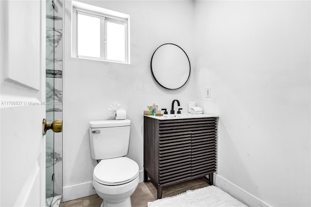 bathroom featuring a shower with shower door, baseboards, vanity, and toilet