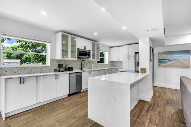 kitchen with wood finish floors, stainless steel appliances, tasteful backsplash, light countertops, and visible vents