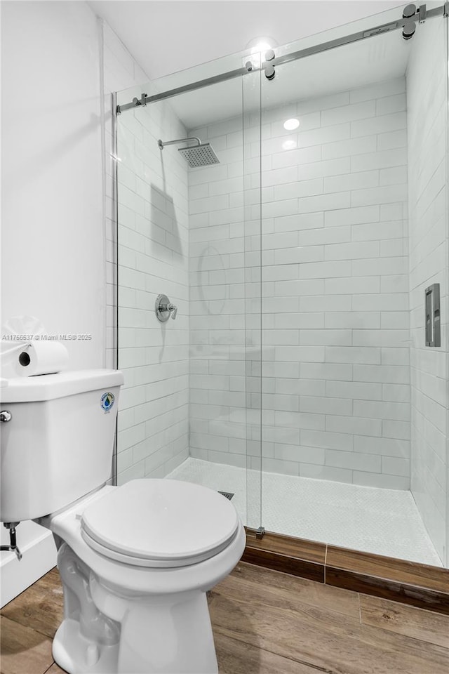 full bath featuring toilet, a stall shower, and wood finished floors