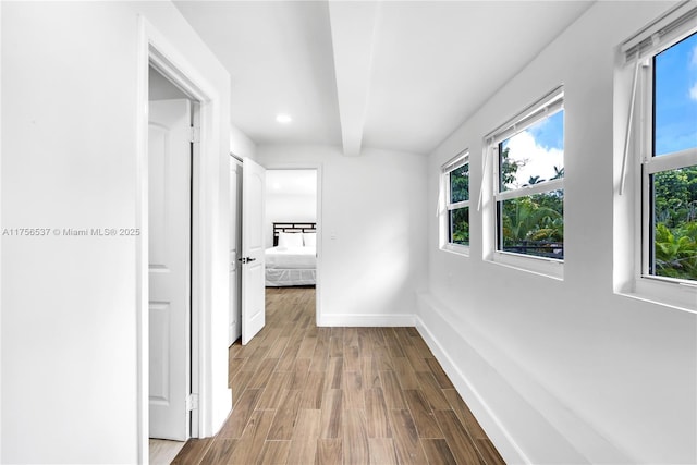 corridor featuring beam ceiling, a healthy amount of sunlight, baseboards, and wood finished floors