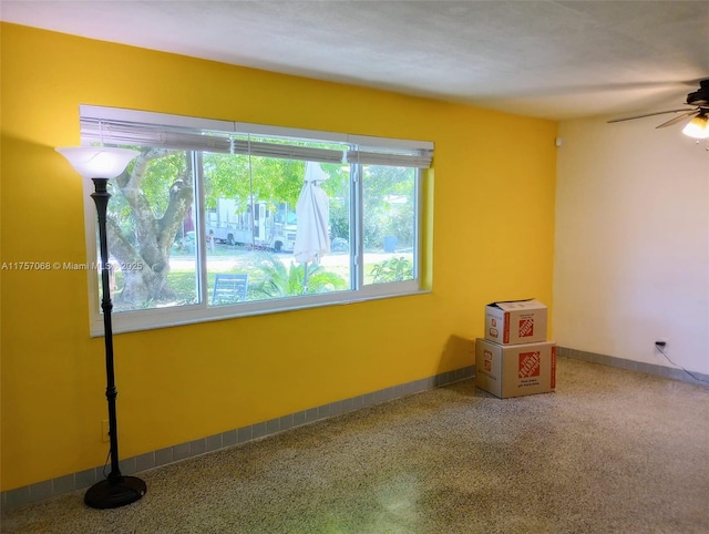 empty room with speckled floor, a ceiling fan, and baseboards