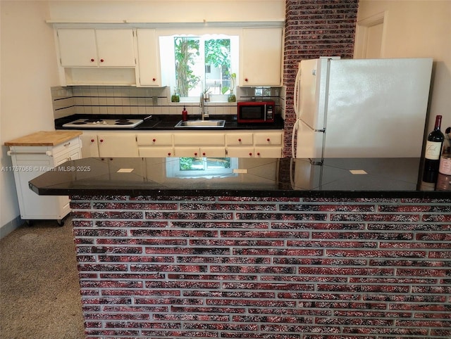 kitchen with dark countertops, backsplash, white cabinetry, a sink, and white appliances