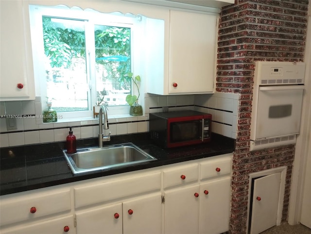 kitchen featuring white cabinets, decorative backsplash, a sink, and oven