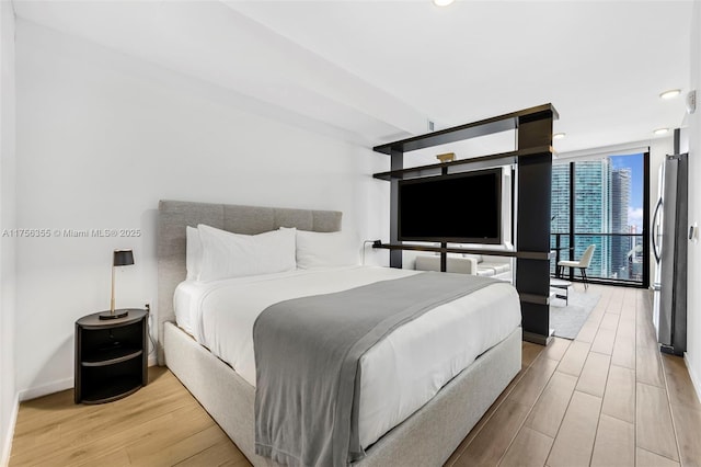 bedroom with light wood finished floors, freestanding refrigerator, and floor to ceiling windows