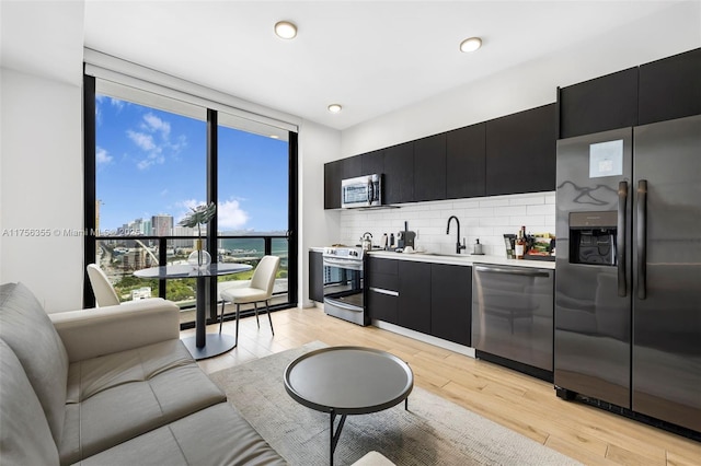 kitchen featuring light wood-style flooring, dark cabinets, stainless steel appliances, a sink, and backsplash