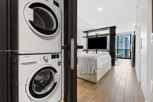 washroom with wood finish floors, stacked washer and clothes dryer, and laundry area