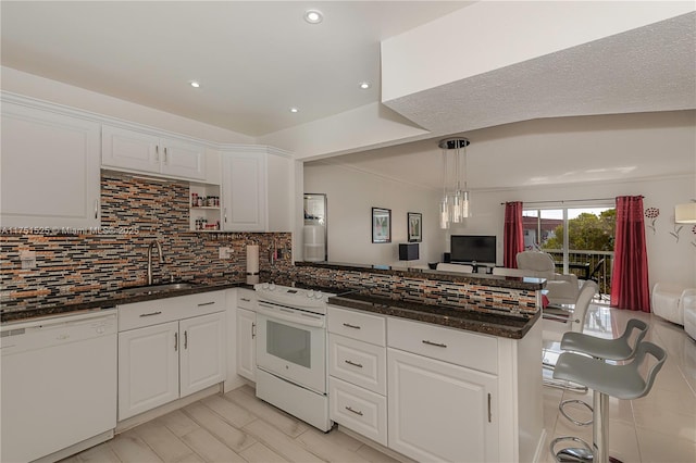 kitchen with a peninsula, white appliances, a sink, open floor plan, and decorative backsplash