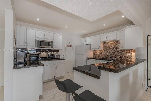 kitchen with backsplash, white cabinets, a sink, white appliances, and a peninsula