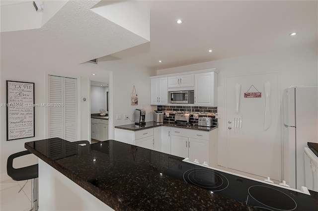 kitchen featuring recessed lighting, white cabinetry, backsplash, freestanding refrigerator, and stainless steel microwave