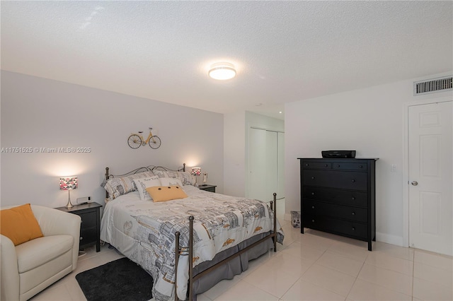 bedroom featuring a textured ceiling, visible vents, a closet, and light tile patterned flooring