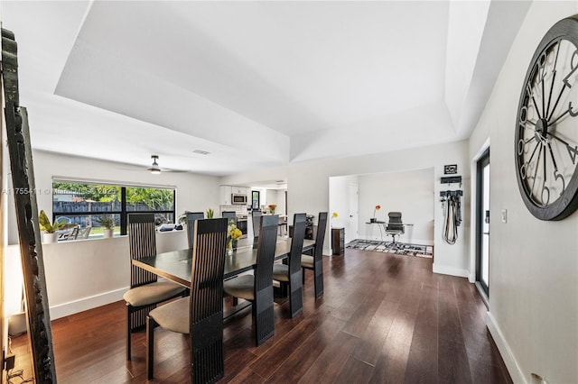 dining area featuring a ceiling fan, a raised ceiling, baseboards, and wood finished floors