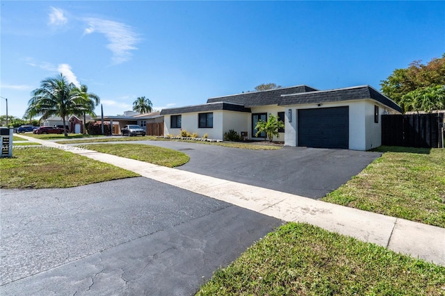 view of front of house with aphalt driveway, a garage, a shingled roof, fence, and a front lawn