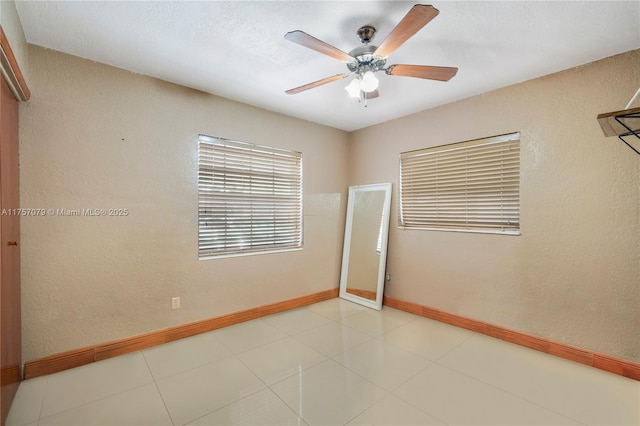 empty room featuring a textured wall, a ceiling fan, and baseboards